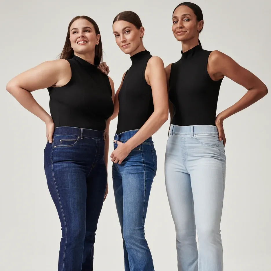 Three women are wearing black sleeveless turtlenecks and different shades of blue jeans.