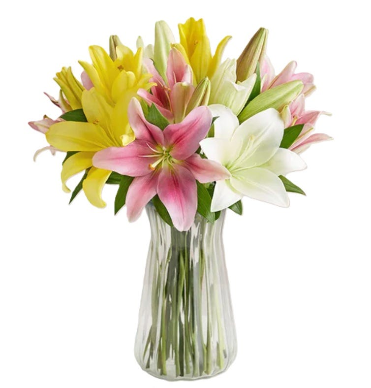 A vibrant bouquet featuring lilies in shades of pink, yellow, and white, arranged in a clear glass vase.