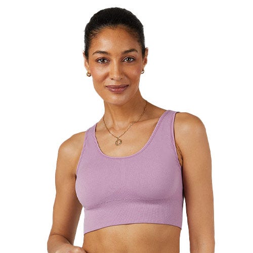 A woman is wearing a lavender sports bra with wide straps and ribbed detailing, paired with small hoop earrings and a gold necklace.