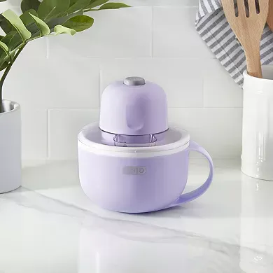 A compact, purple Dash Mug Ice Cream Maker with a handle is displayed on a kitchen counter, designed to make personal-sized servings of ice cream.
