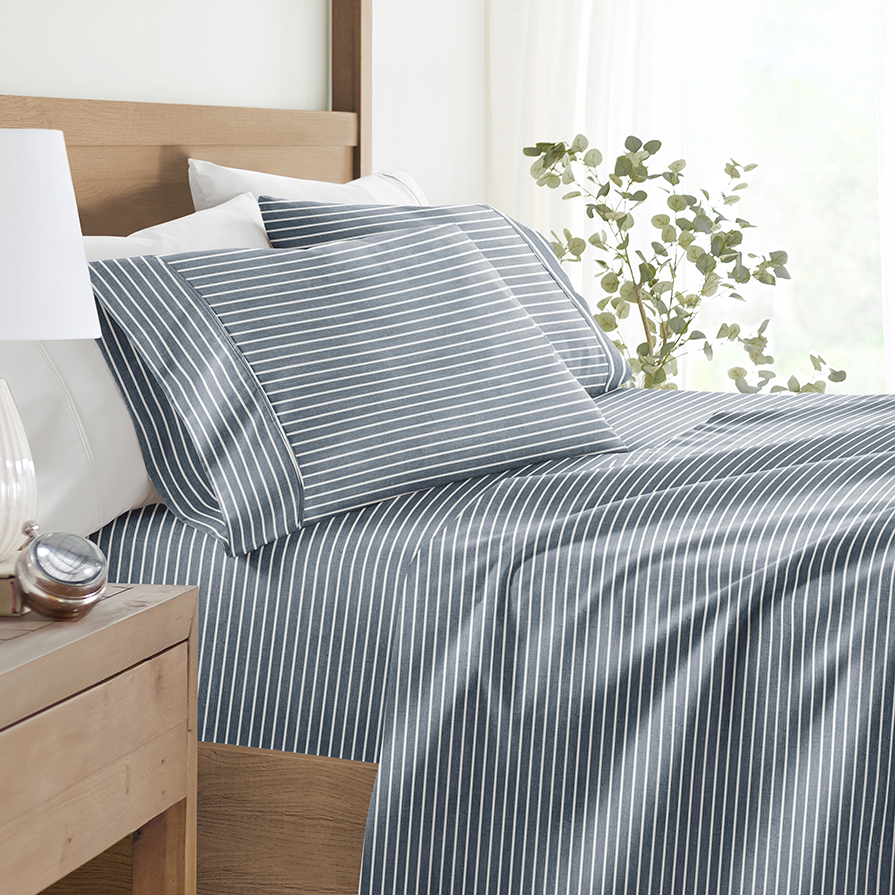 Striped bedding set with pillowcases and sheets on a bed, next to a nightstand with a lamp and plant.
