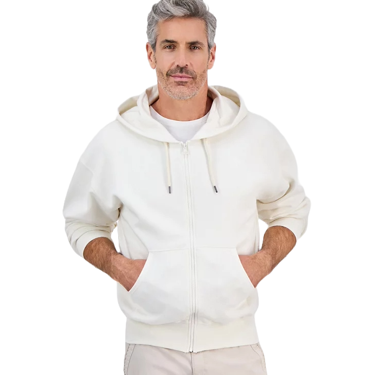 A man wears a white zip-up hoodie with a front pocket and drawstrings, paired with light-colored pants.