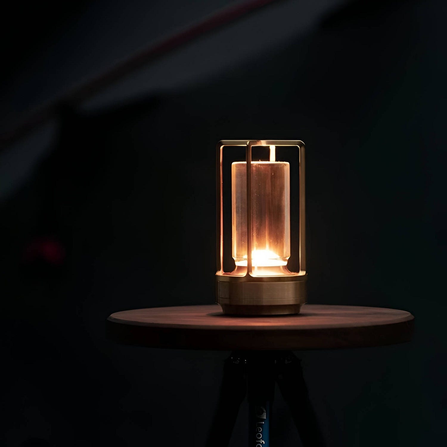 A cylindrical table lamp with a warm, Edison-style filament bulb on a wooden tripod stand.
