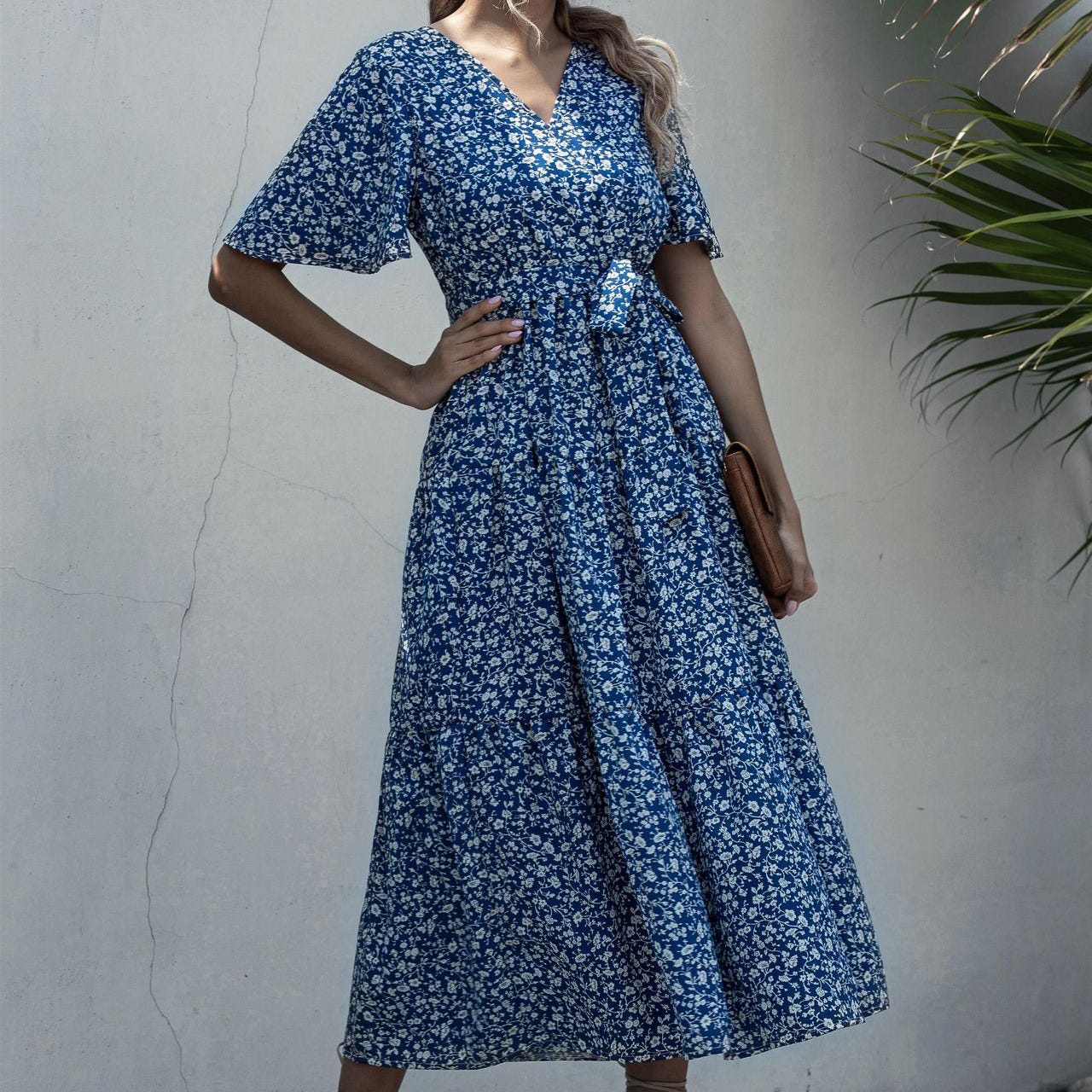 A woman is wearing a blue and white floral print mid-length dress with short sleeves, a V-neckline, and a tied waist.