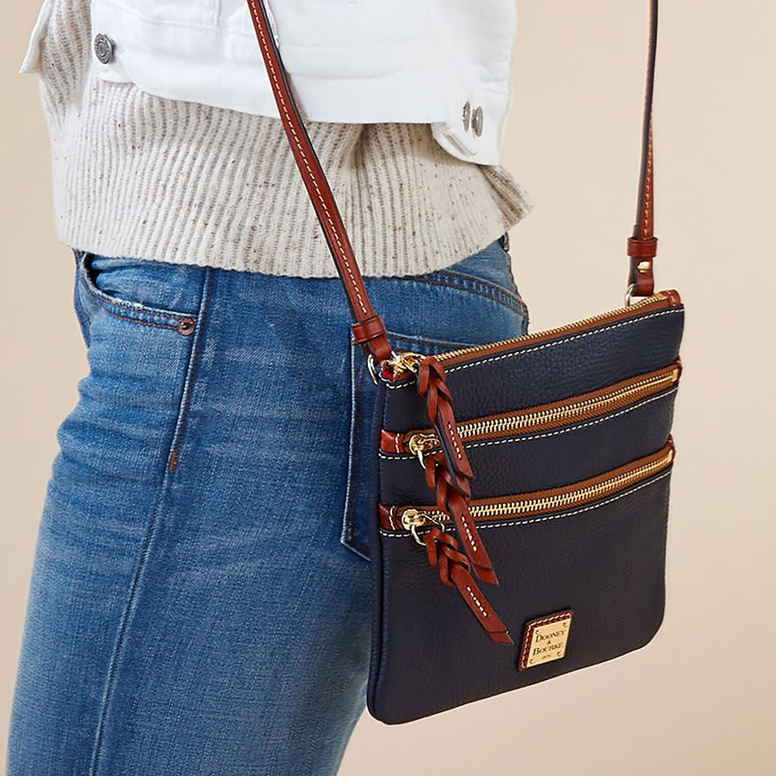 A navy crossbody bag with multiple front zip compartments and a brown leather strap.