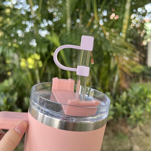 A silicone straw topper in the shape of a heart with a slot for a straw is attached to a clear straw in a pink insulated tumbler.