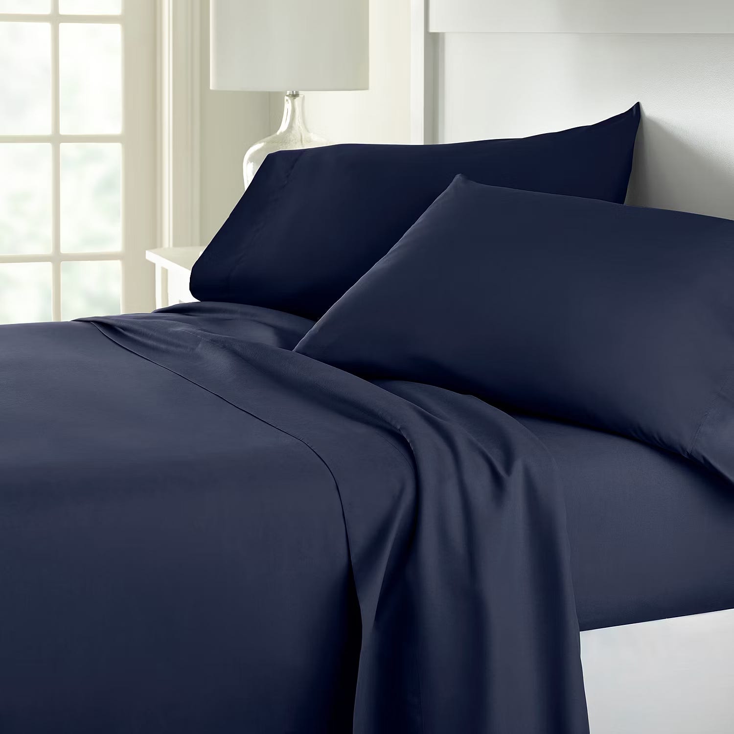 A navy blue bed sheet set with pillowcases on a bed near a window.