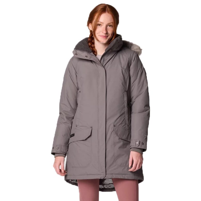 A woman wearing a gray winter parka with a fur-lined hood and large front pockets, paired with pink leggings.