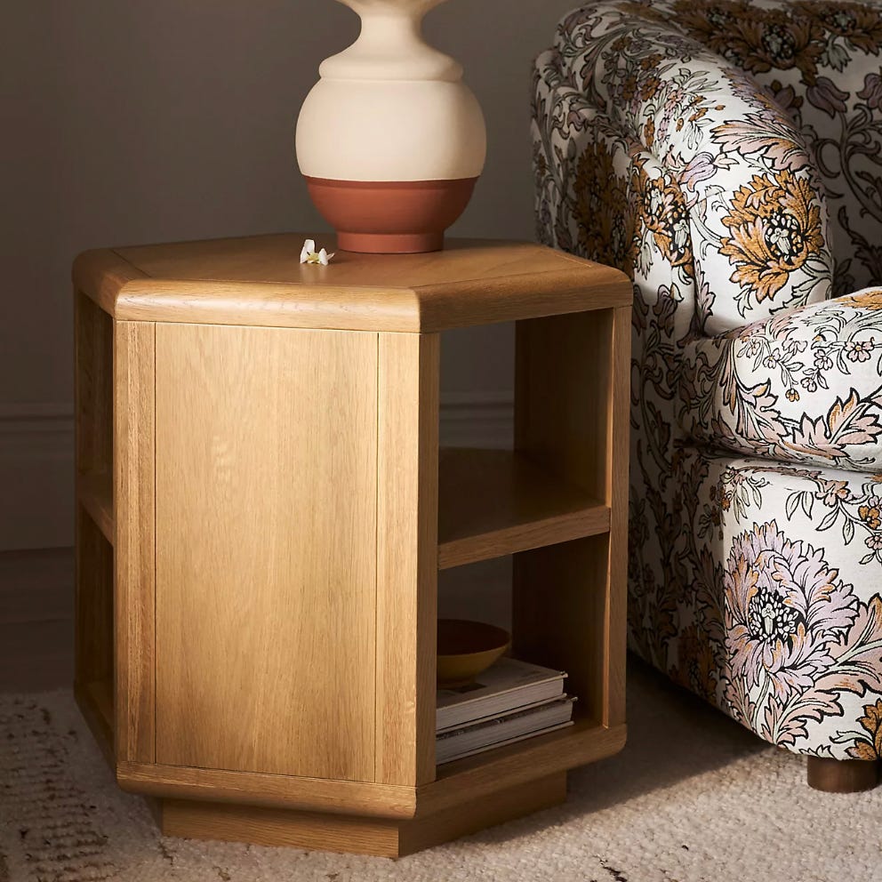 Wooden side table with open shelving, featuring a decorative vase on top and placed beside a floral-patterned couch.