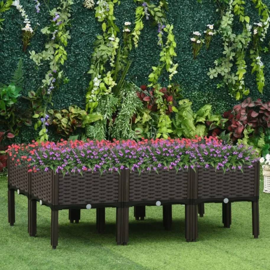 Raised garden bed with purple and red blossoms set against a backdrop of a lush green artificial leaf wall.