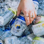 A hand is reaching into a pile of crushed ice to grab a can of Waterloo Blackberry Lemonade, surrounded by more cans of the same and different flavors.