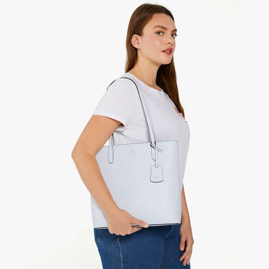 A woman is wearing a white T-shirt and blue jeans, carrying a white tote bag over her shoulder.