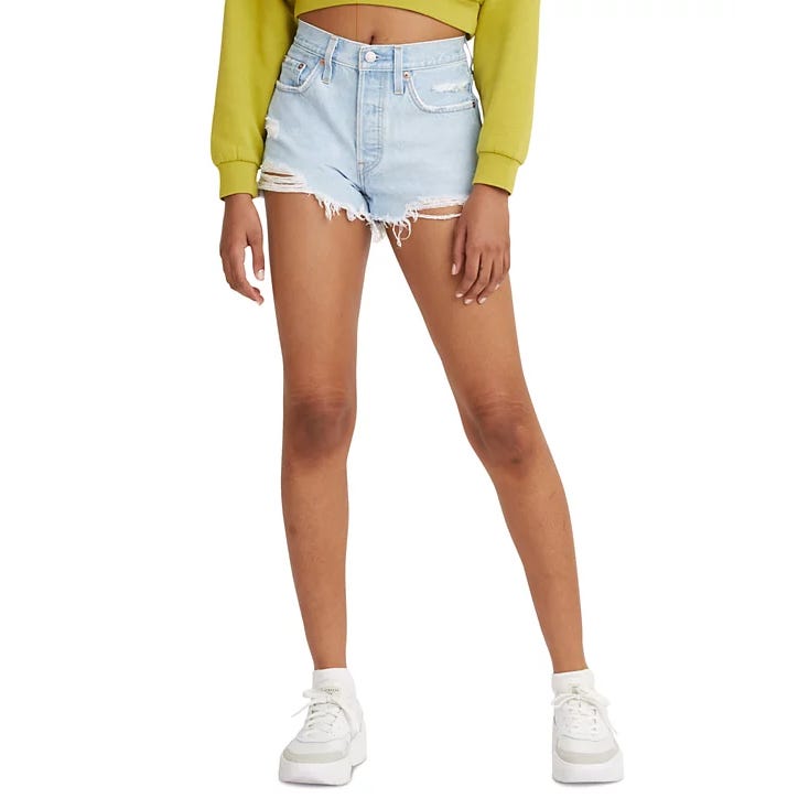 Light denim high-waisted distressed shorts with frayed hems, paired with white sneakers and a long-sleeve green top.