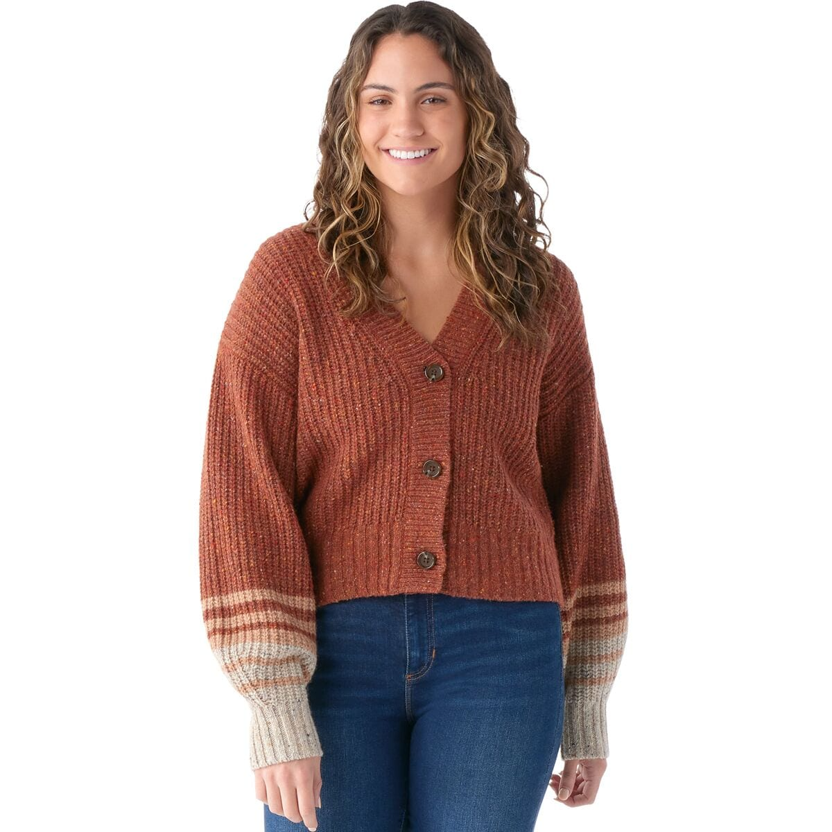 A smiling woman wearing a rust-toned knitted cardigan with striped cuffs and blue jeans.