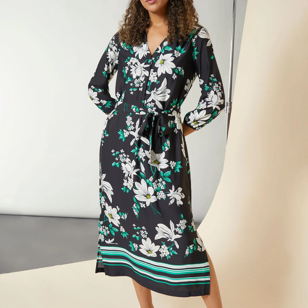 Black V-neck dress with white and green floral patterns and horizontal green stripes near the hem.