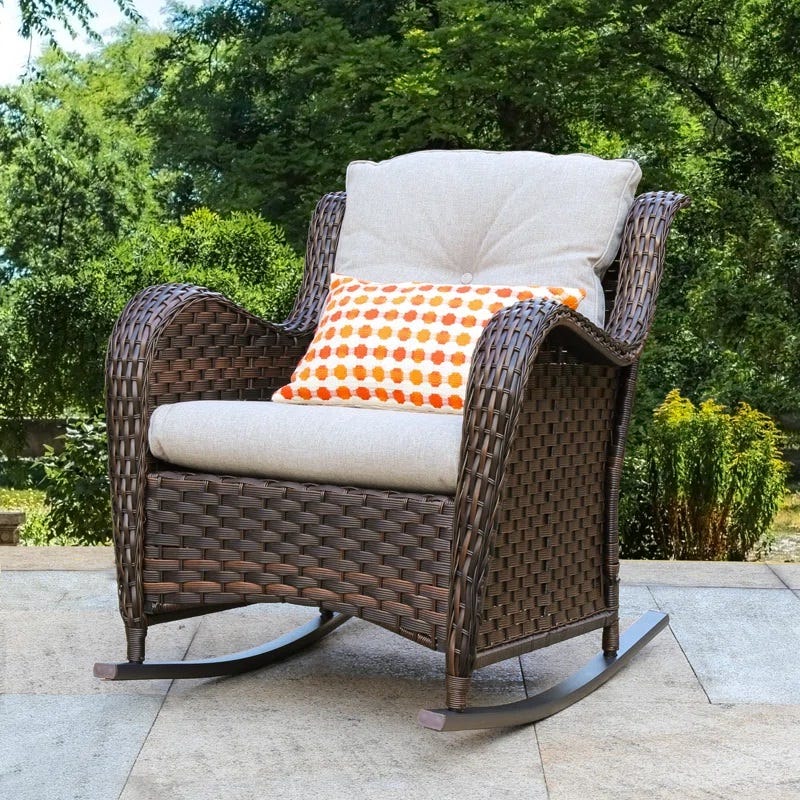 Wicker rocking chair with beige cushions and an orange polka dot pillow, placed on an outdoor patio.