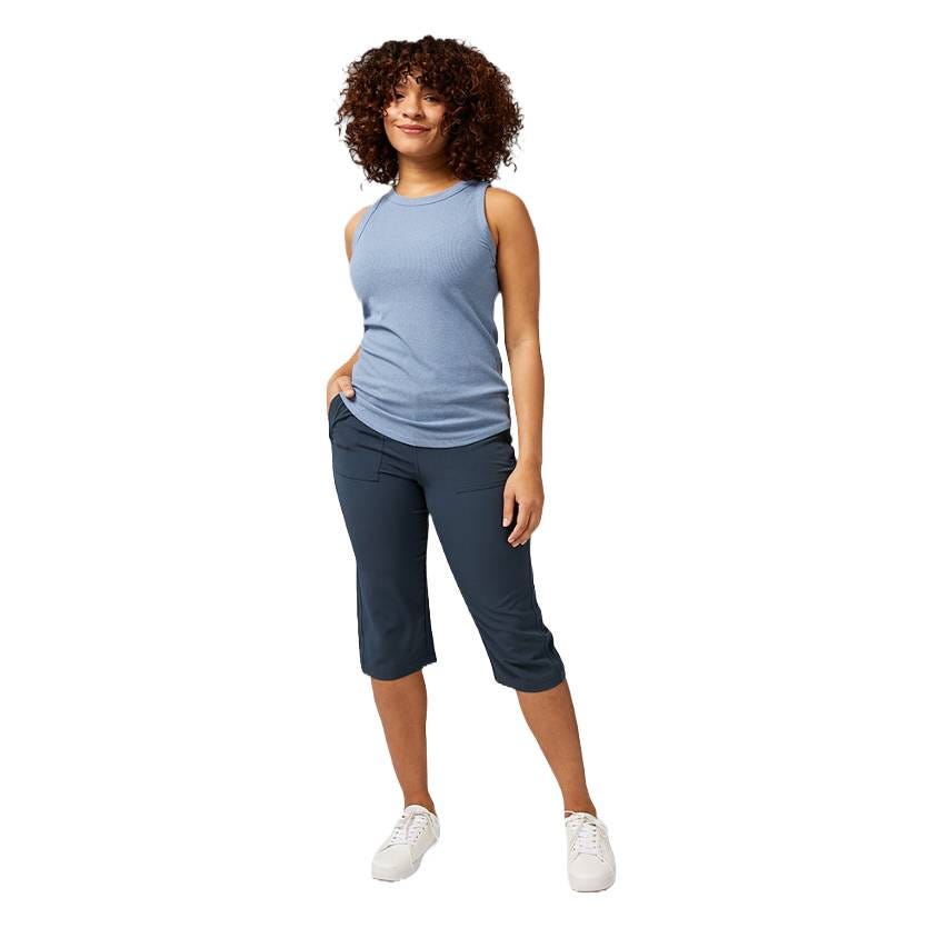 A person wearing a light blue sleeveless top, dark knee-length pants with pockets, and white sneakers.