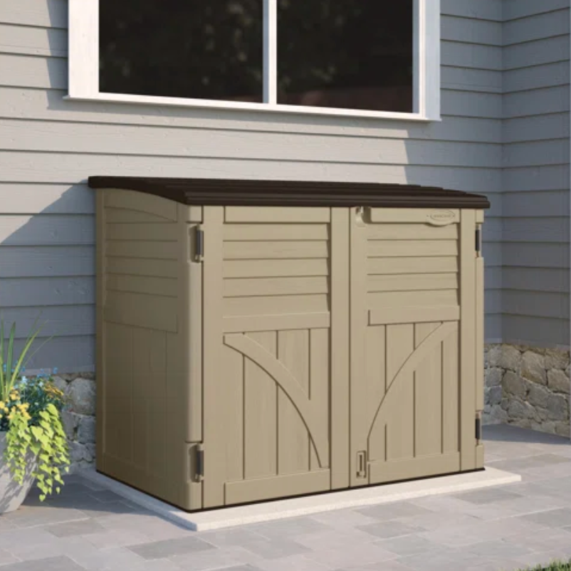Beige outdoor storage shed with double doors, positioned against a house near a window.