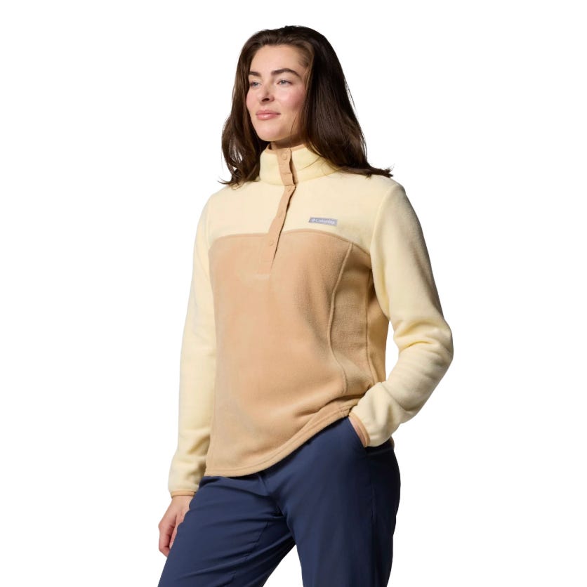 A person is wearing a Patagonia pullover fleece jacket in beige and cream with blue pants. The jacket features a snap-button collar and a patch logo on the chest.