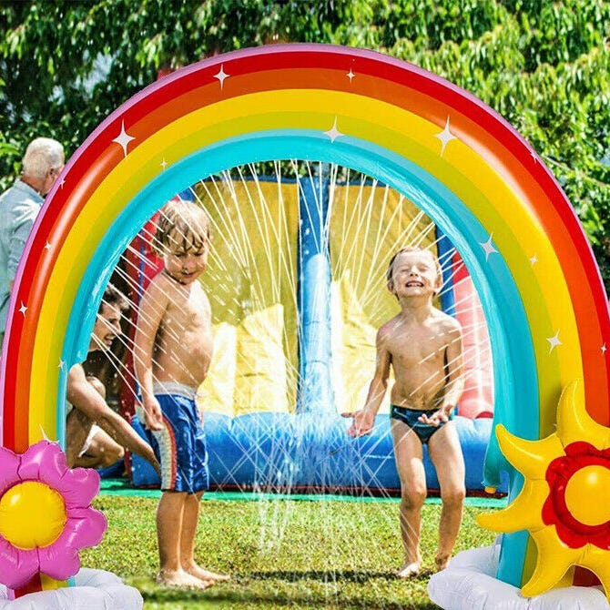 An inflatable rainbow-shaped water sprinkler toy with two children playing underneath.
