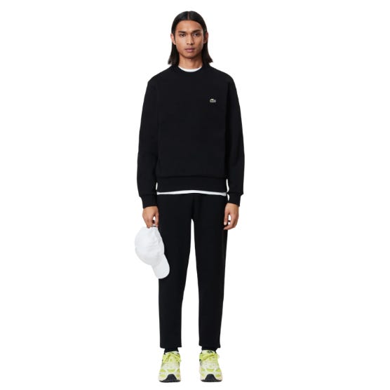Lacoste Men's Tapered Sweatpants in black feature a minimalist design with a comfortable fit, elastic waistband, and ribbed cuffs. Paired with matching sweatshirt and lime green sneakers, the look is casual and sporty.
