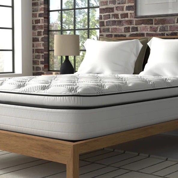 A mattress with a patterned pillow-top design on a wooden bed frame, accompanied by white pillows and a table lamp.