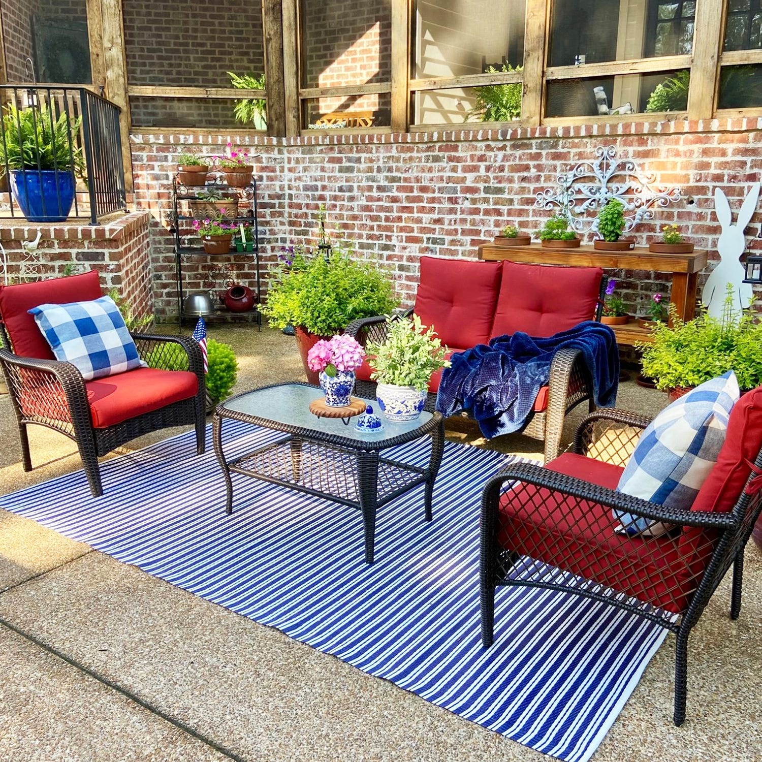 Outdoor patio furniture set with red cushions, a striped rug, and decorative plants.