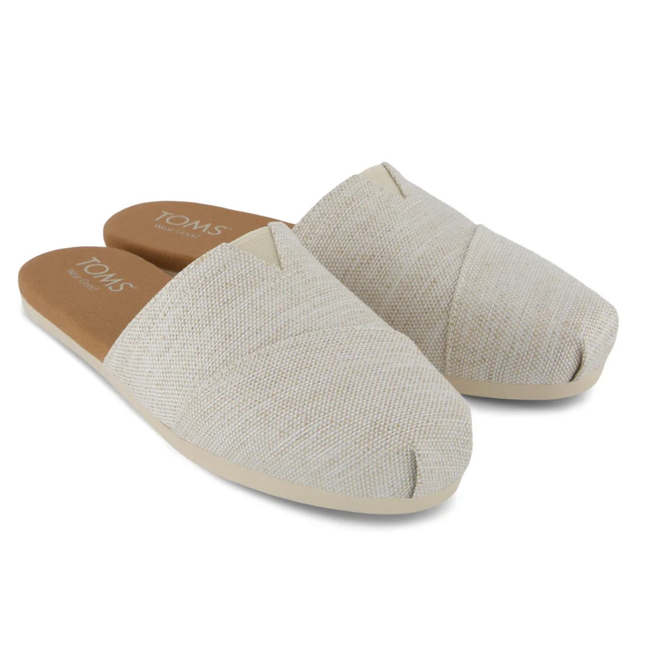 Beige TOMS mules with a slip-on design featuring a cross-stitch detail on the upper, made from textured fabric. They have flat soles with light brown insoles.