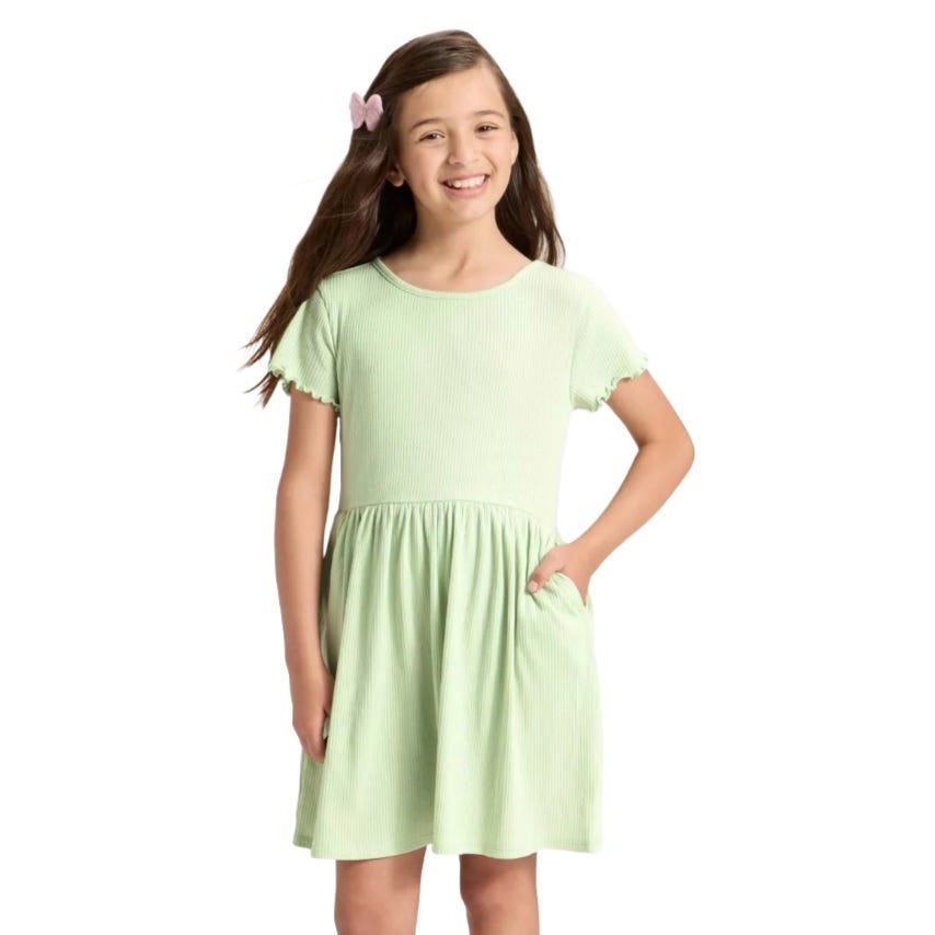 A young girl models a light green short-sleeved dress with a gathered waist and ruffled sleeves, featuring a pocket and a pink hair clip.