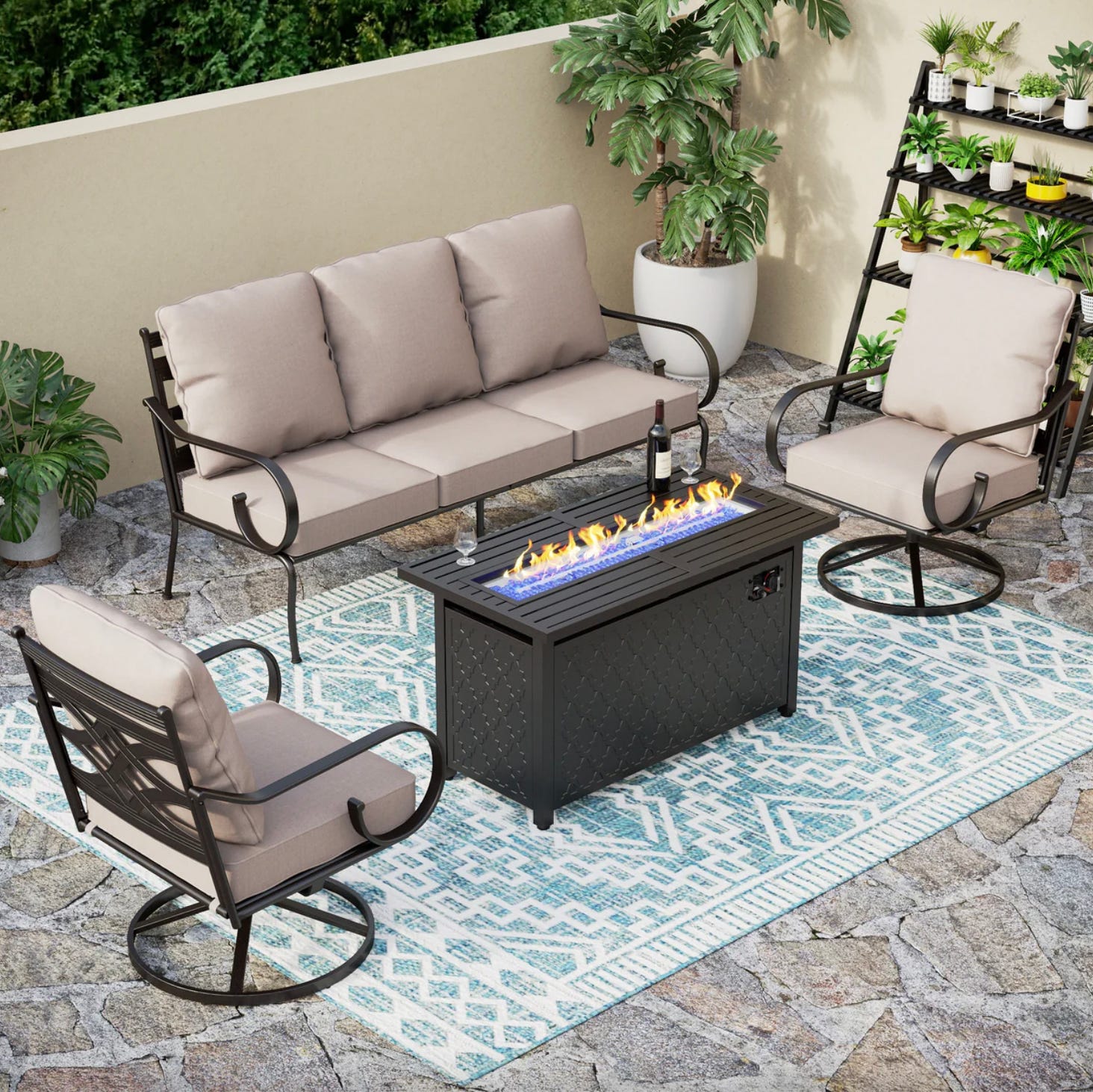 A five-seater patio set featuring a three-person sofa, two swivel chairs, and a rectangular fire pit table, complemented by a blue and white outdoor rug and surrounded by potted plants.