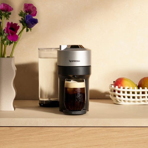 Nespresso coffee machine next to a glass of water and a fruit basket.
