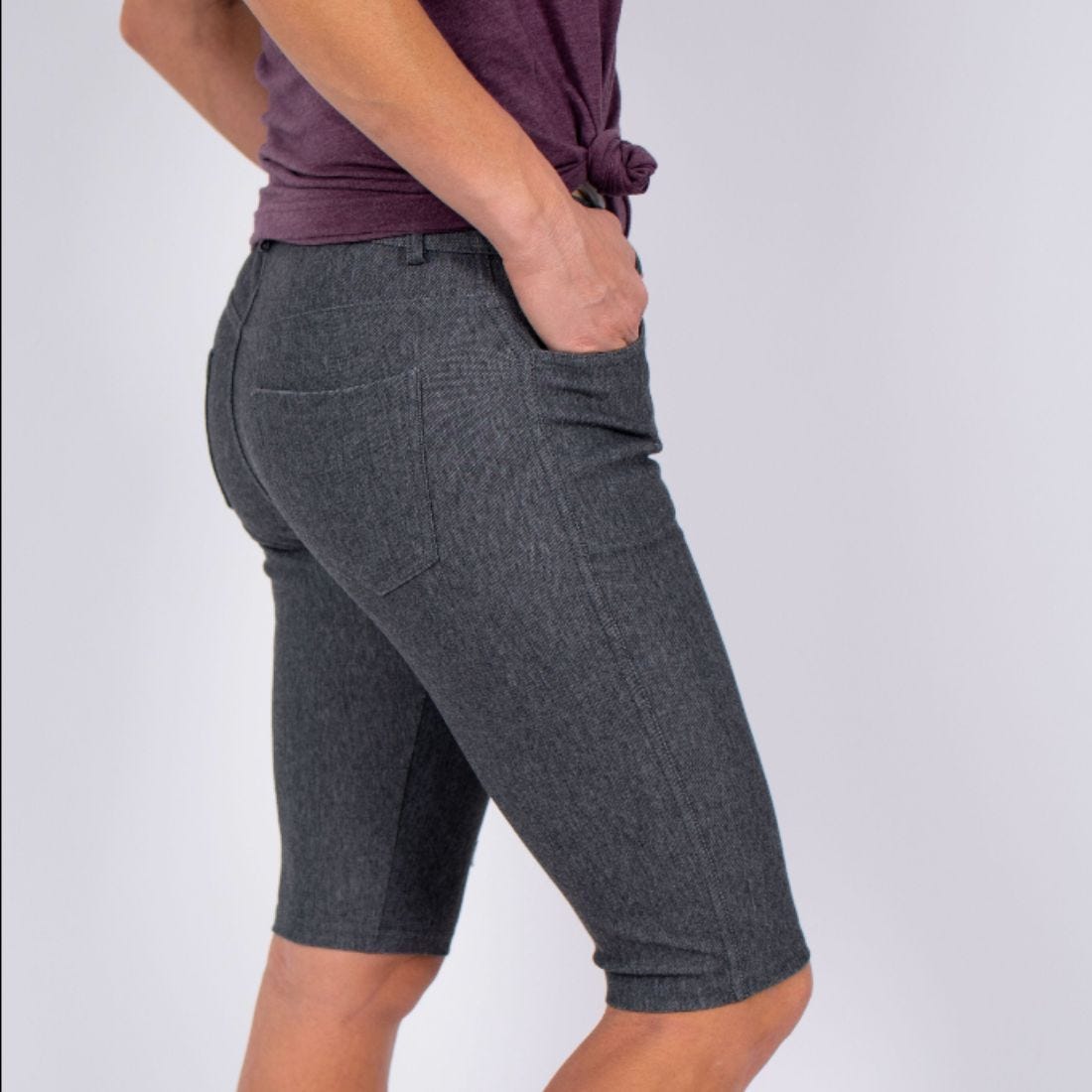 A person wearing grey denim bermuda shorts and a purple top.
