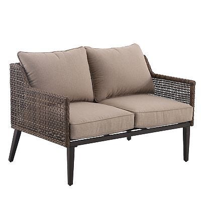 A patio loveseat with beige cushions and a dark woven wicker frame.