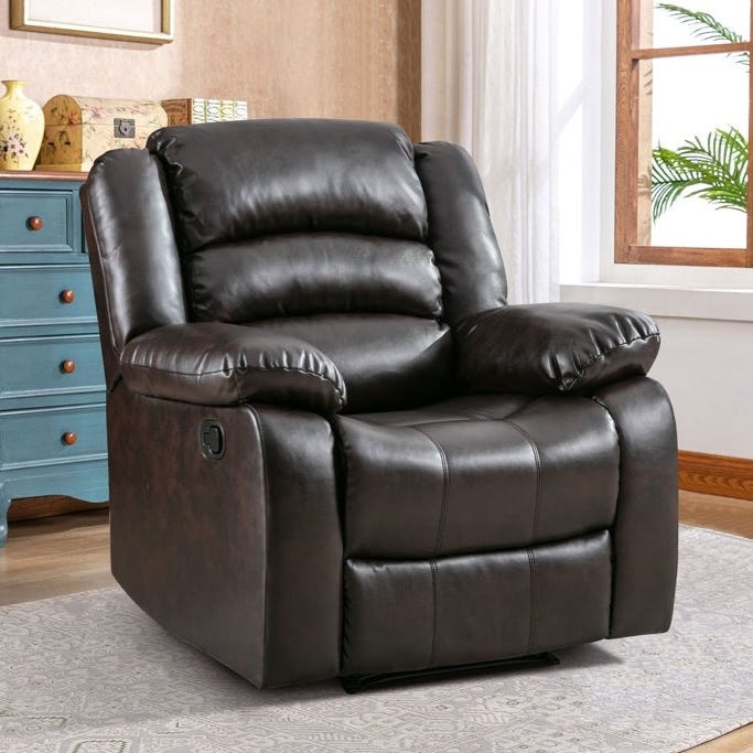 A dark brown leather recliner chair with padded armrests and a cushioned backrest is placed on a patterned rug in a room with a blue dresser and a window.