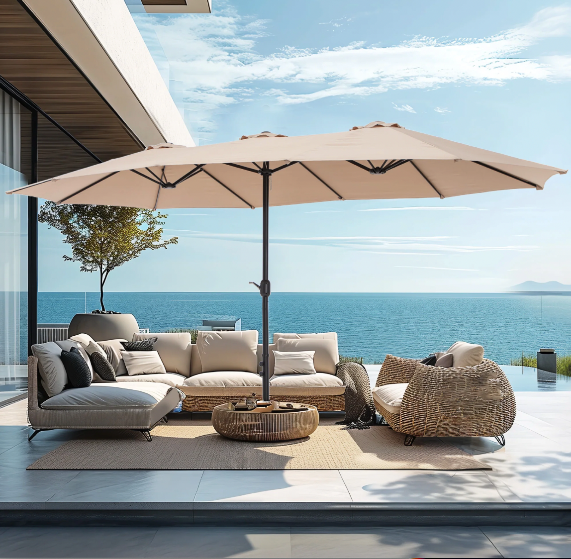 A large beige patio umbrella with a sturdy black base provides ample shade over outdoor wicker furniture. It's set on a modern patio with a scenic ocean view.