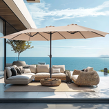 A large beige patio umbrella with a sturdy black base provides ample shade over outdoor wicker furniture. It's set on a modern patio with a scenic ocean view.