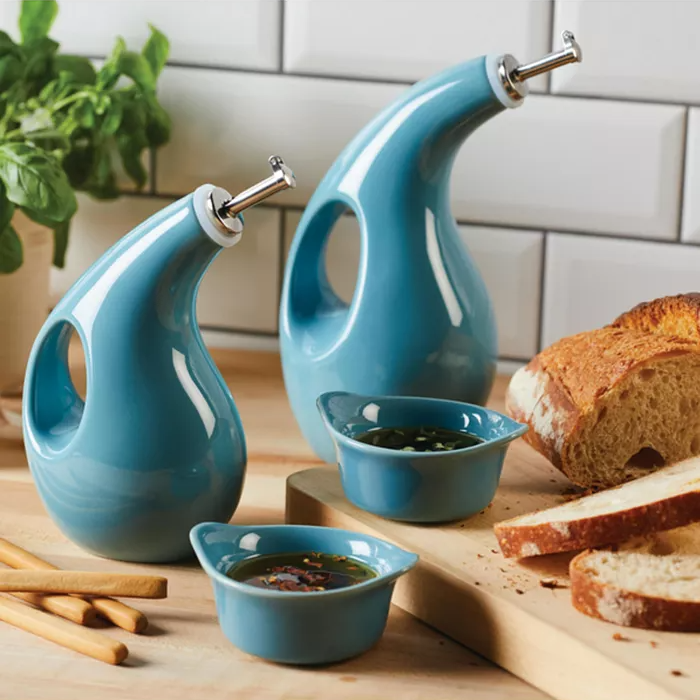 Two unique blue oil and vinegar dispensers with swan-neck spouts and matching dipping bowls on a kitchen counter.