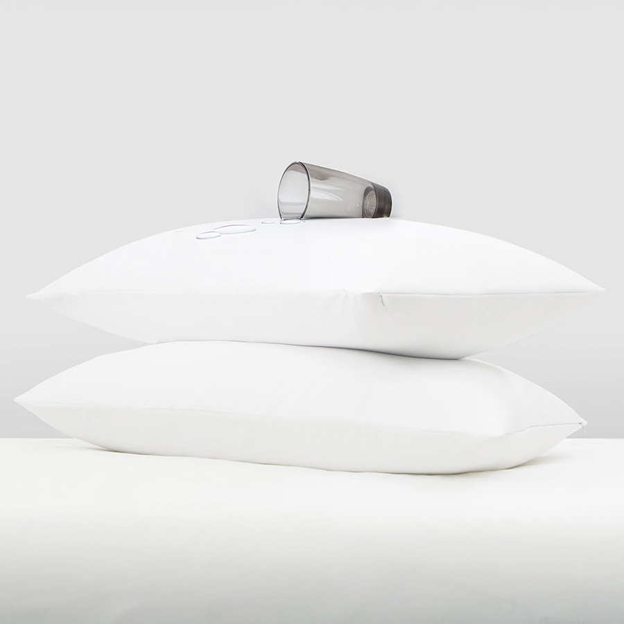 Two stacked white pillows with a clear glass of water resting on top.