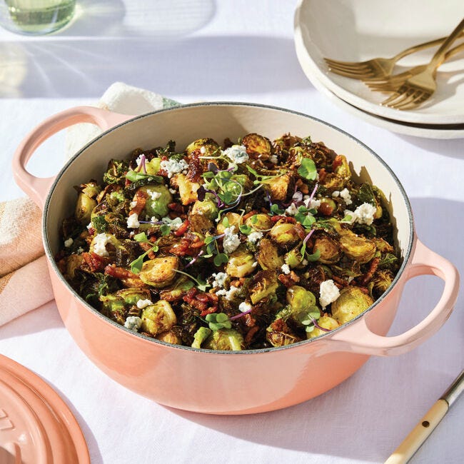 A dish of roasted Brussels sprouts with pecans and herbs served in a peach-colored casserole pot.
