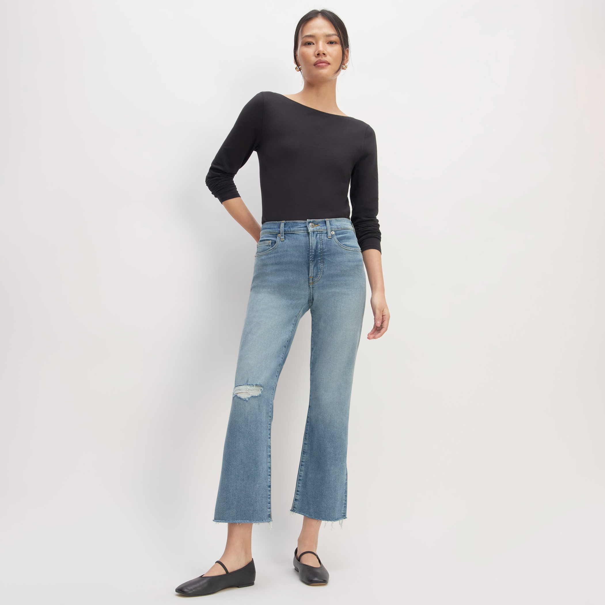 A woman is wearing light blue ripped jeans, a long-sleeve black top, and black flats.
