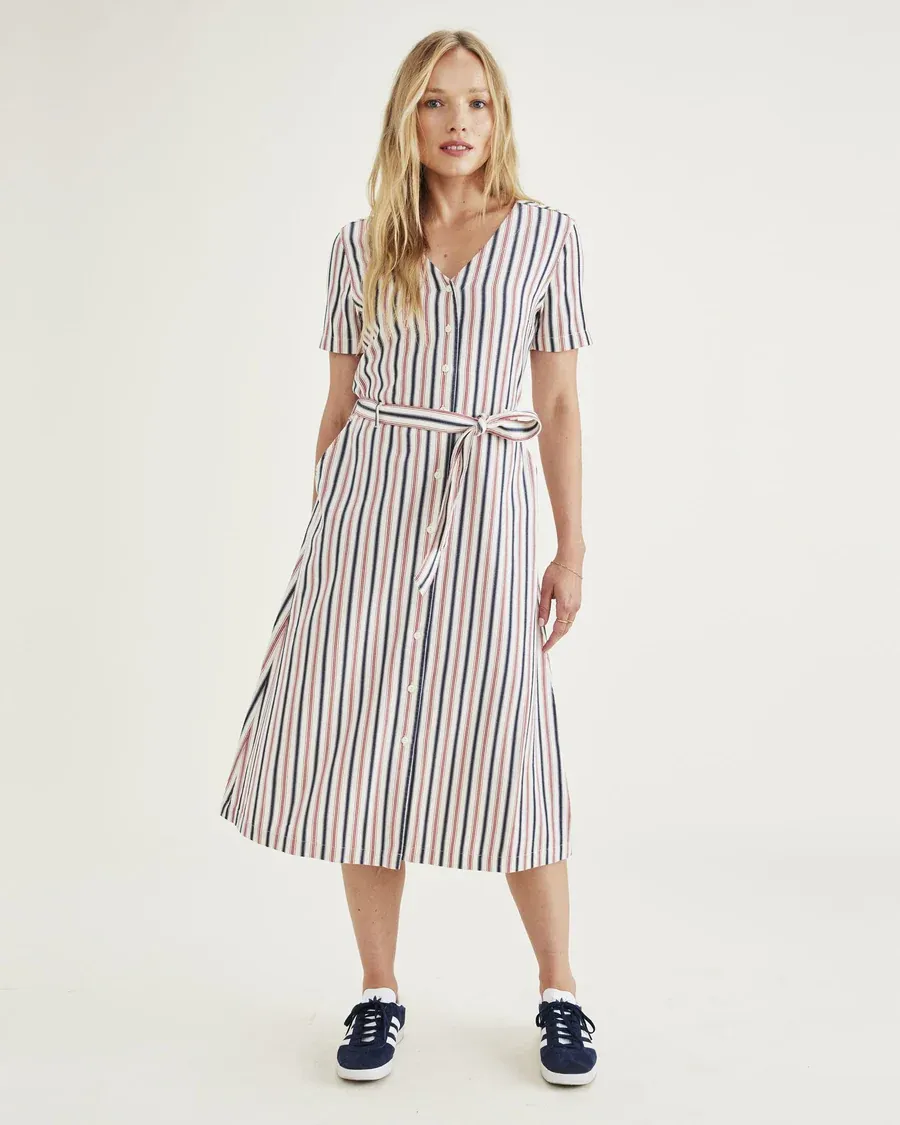 A woman wearing a striped mid-length dress with a belt and navy blue sneakers.