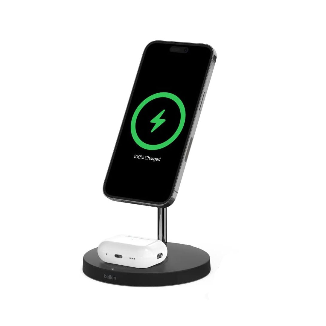 Refurb Belkin 2-in-1 Charging Stand holds a smartphone vertically and wirelessly charges it alongside an AirPods case. The base is circular and features a sleek design with a brand logo.