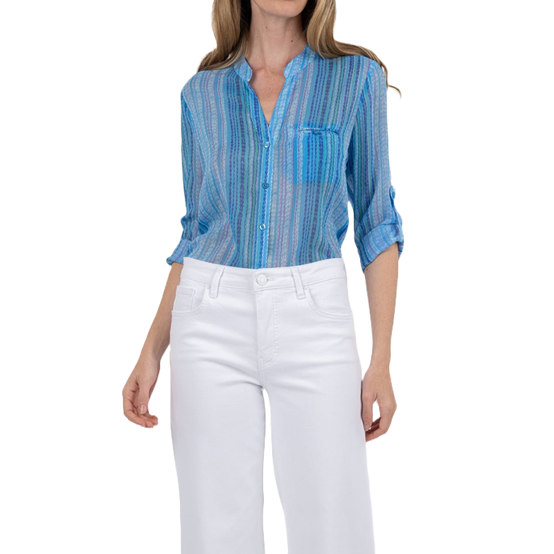 A woman is wearing a blue, striped button-up shirt with rolled-up sleeves and white pants.