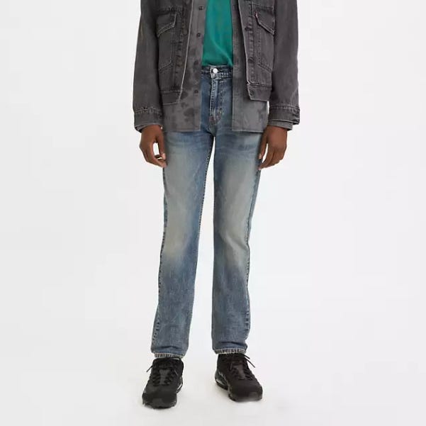 A person wearing a gray denim jacket, blue jeans, teal top, and black sneakers.