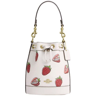 A white Coach Outlet bucket bag with a drawstring closure and gold hardware, featuring a playful strawberry print.
