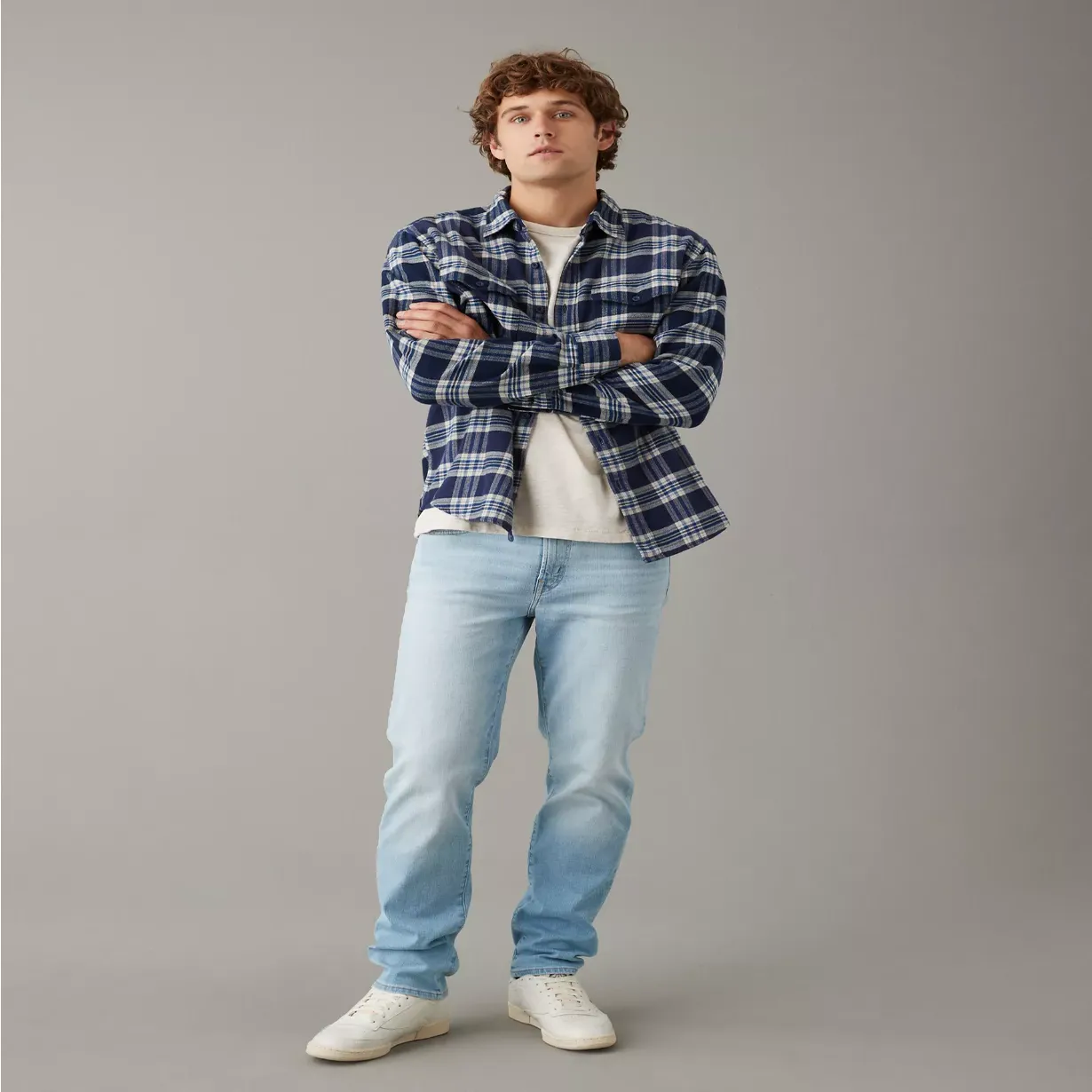 A man wearing a blue and white plaid shirt, white t-shirt, light blue jeans, and white sneakers.