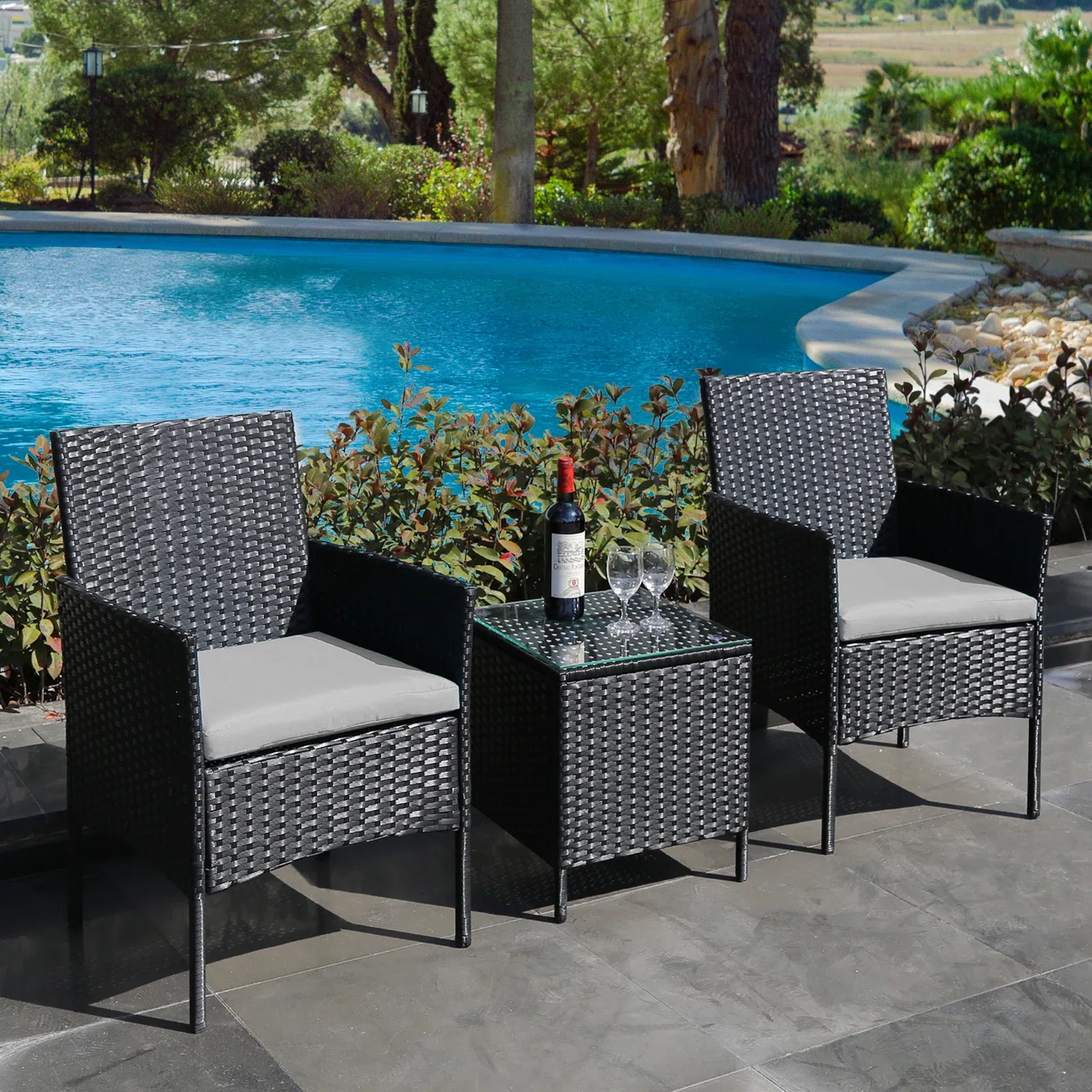 Three-piece outdoor furniture set with two wicker chairs and a matching side table, accompanied by a bottle of wine and two glasses.