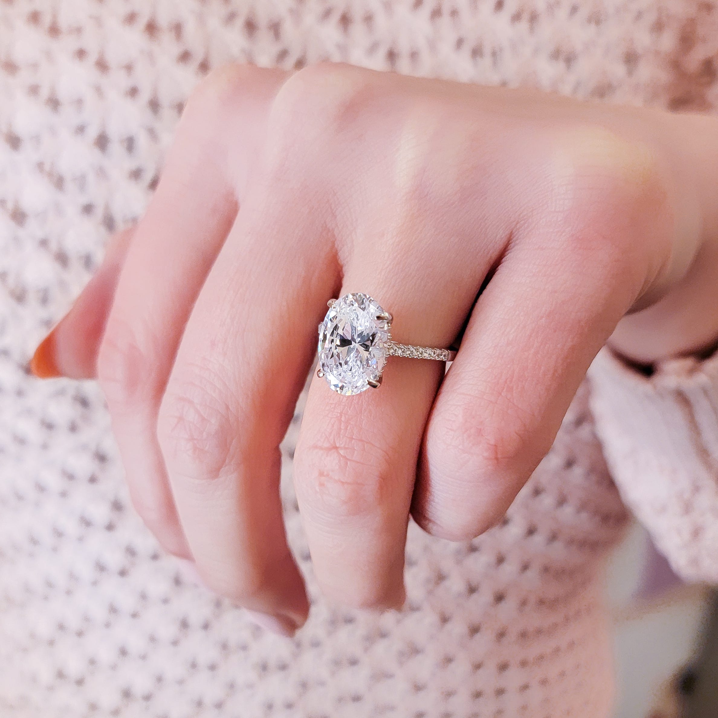A hand wearing an oval-cut diamond engagement ring, with smaller diamonds encrusted on the band.