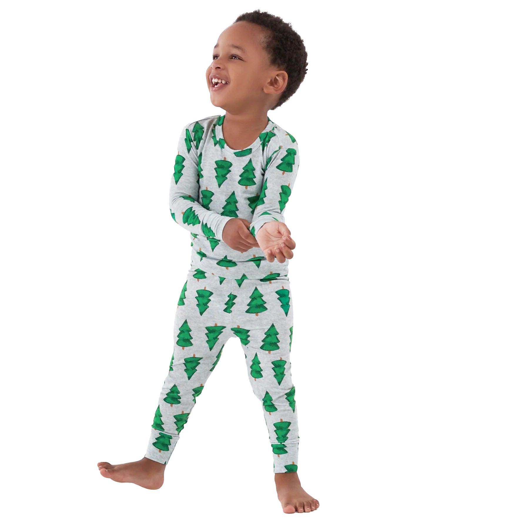 The Gerber Holiday Pajama Sets feature a child wearing matching long-sleeve top and pants with a festive green Christmas tree pattern on a light gray background.