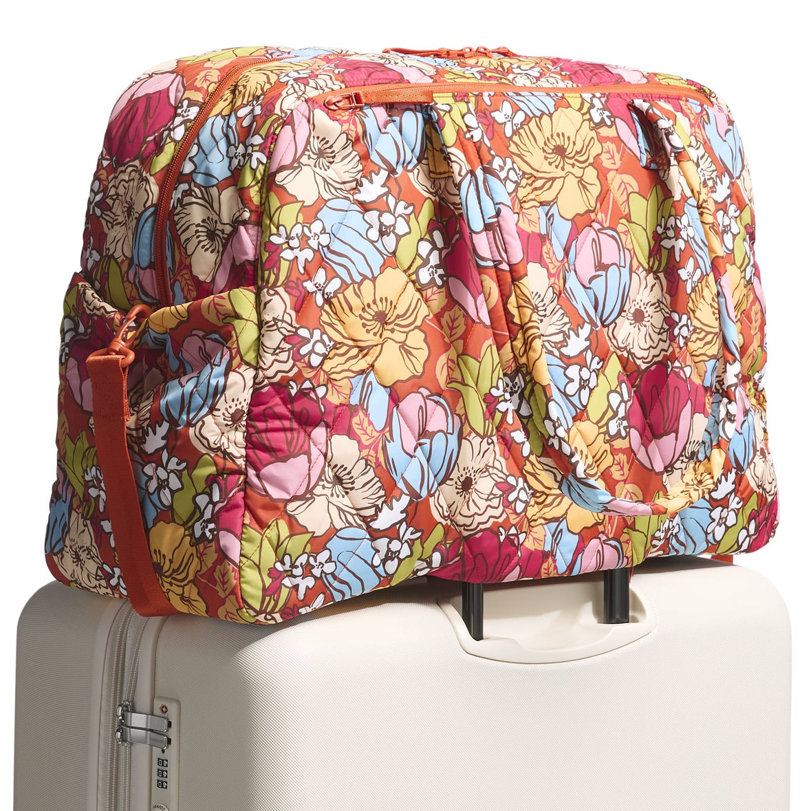 Vera Bradley Large Weekender Bag featuring a colorful floral pattern with red, blue, yellow, pink, and green tones; shown resting atop a cream-colored rolling suitcase.